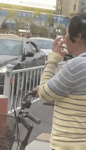A Woman Smoking A Cigarette While Standing Next To A Bike GIF