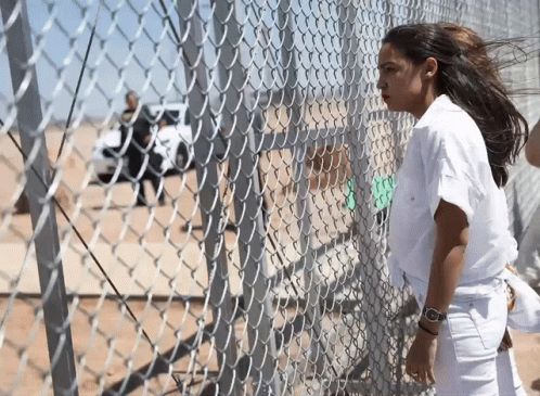 A Woman Standing Behind A Chain Link Fence With A Watch On Her Wrist GIF