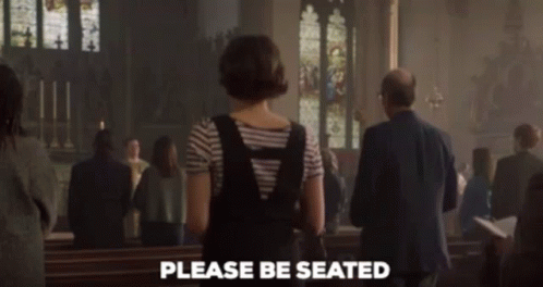 A Woman Standing In A Church With The Words Please Be Seated Written On The Bottom GIF