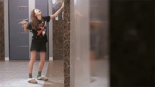 A Woman Standing In A Hallway With A Door That Says Hh GIF