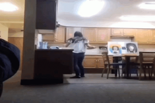 A Woman Standing In A Kitchen With A Painting Of A Woman On The Wall GIF