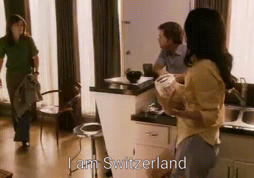 A Woman Standing In A Kitchen With The Words I Am Switzerland Written Above Her GIF