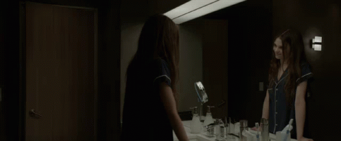 A Woman Standing In Front Of A Bathroom Mirror GIF