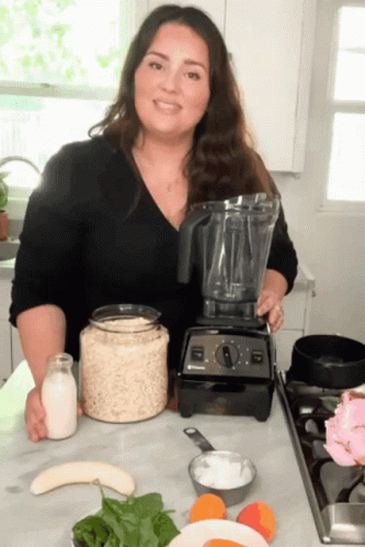 A Woman Standing In Front Of A Blender With A Bottle Of Milk On The Counter GIF