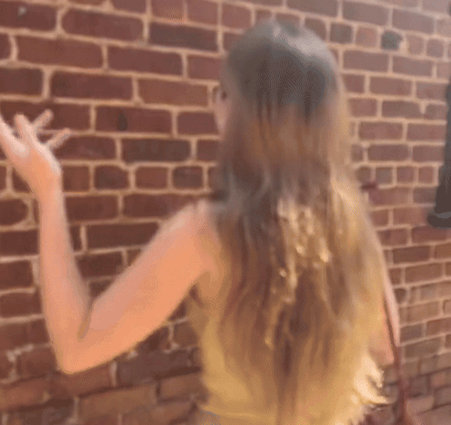 A Woman Standing In Front Of A Brick Wall GIF