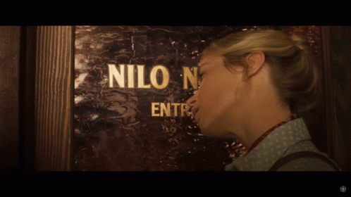 A Woman Standing In Front Of A Door That Says Nilo GIF