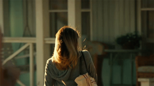 A Woman Standing In Front Of A Porch Holding A Bag GIF