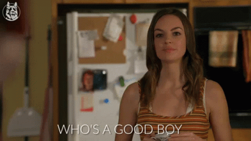 A Woman Standing In Front Of A Refrigerator With The Words Who 'S A Good Boy GIF