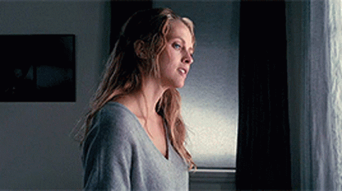 A Woman Standing In Front Of A Window Looking Out GIF