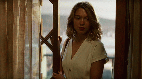 A Woman Standing In Front Of A Window Looking Out GIF