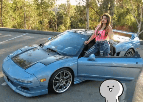 A Woman Standing Next To A Blue Sports Car With The Door Open GIF