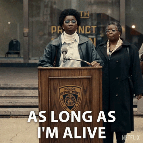 A Woman Stands At A Podium With The Words " As Long As I 'M Alive " Below Her GIF