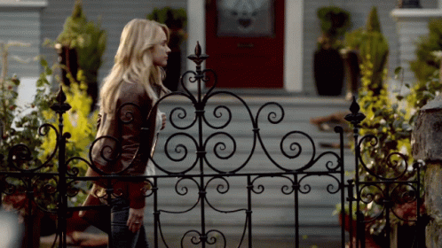 Woman Behind Wrought Iron Fence In Front Of House GIF