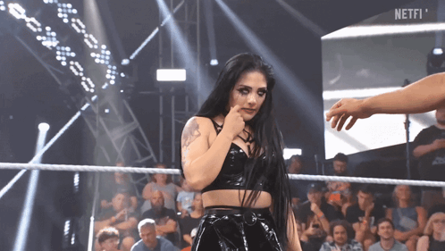 A Woman Stands In A Wrestling Ring With The Word Netfi On The Screen Behind Her GIF