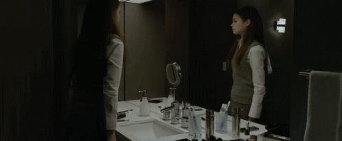 A Woman Stands In Front Of A Bathroom Mirror GIF