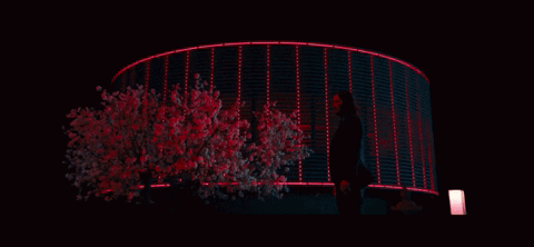 a woman stands in front of a building that is lit up with red lights