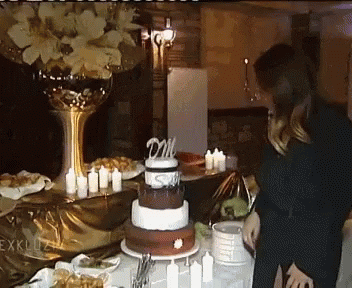 A Woman Stands In Front Of A Cake With A Topper That Says Dm On It GIF
