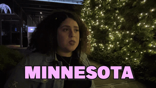 A Woman Stands In Front Of A Christmas Tree With The Word Minnesota On The Bottom GIF