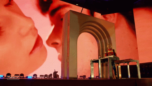 A Woman Stands In Front Of A Large Screen That Says " Coachella " On It GIF