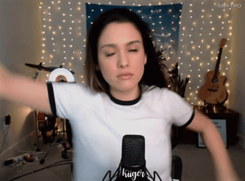 A Woman Stands In Front Of A Microphone That Says " Kiiger " On It GIF