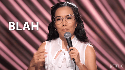 A Woman Stands In Front Of A Microphone With The Word Blah Behind Her GIF