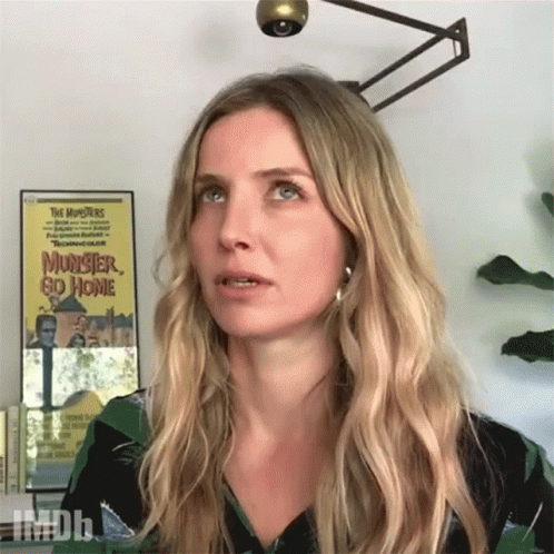 A Woman Stands In Front Of A Poster For The Movie Monster Go Home GIF