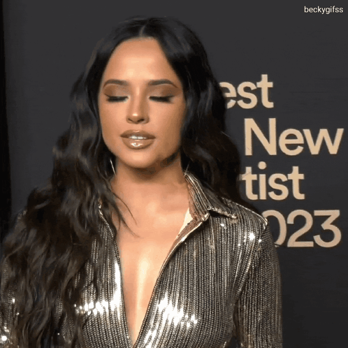 A Woman Stands In Front Of A Sign That Says " Best New Tist " GIF