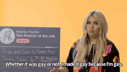 A Woman Stands In Front Of A Sign That Says Hayley Kiyoko The Playlist Of My Life GIF