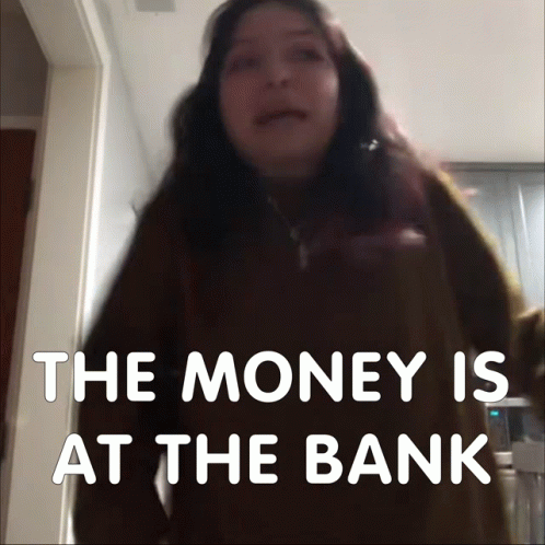 A Woman Stands In Front Of A Sign That Says " The Money Is At The Bank " GIF