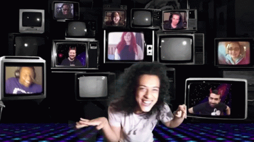 A Woman Stands In Front Of A Wall Of Televisions Including One That Says S2 On It GIF