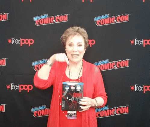 A Woman Stands In Front Of A Wall That Says Comic Con On It GIF