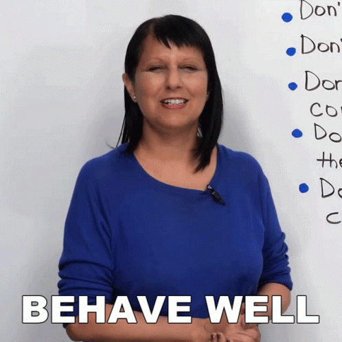 A Woman Stands In Front Of A White Board That Says Behave Well GIF