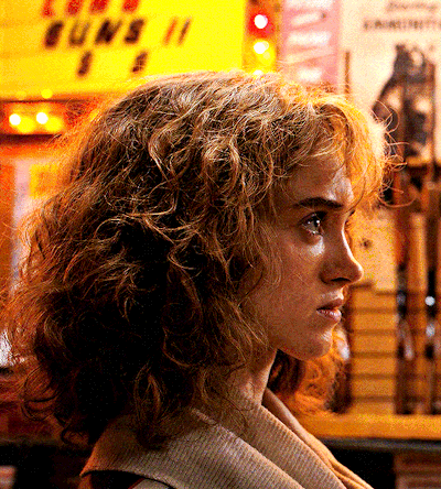 A Woman Stands In Front Of A Yellow Sign That Says Guns GIF
