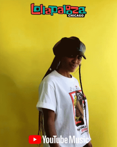 A Woman Stands In Front Of A Yellow Wall That Says ' Lolapaloza Chicago ' GIF