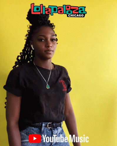 A Woman Stands In Front Of A Yellow Wall With A Lolapaloza Chicago Logo On It GIF