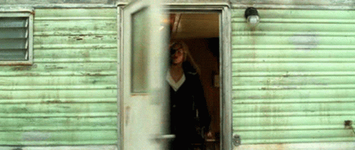 A Woman Stands In The Doorway Of A Green Trailer GIF