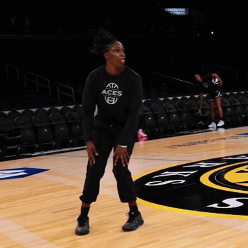 A Woman Stands On A Basketball Court Wearing A Black Aces Shirt GIF