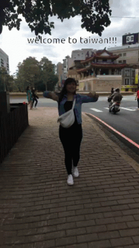 A Woman Stands On A Brick Sidewalk With Her Arms Outstretched And The Words Welcome To Taiwan Written Below Her GIF