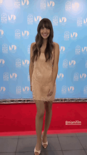 A Woman Stands On A Red Carpet In Front Of A Backdrop That Says Miamifilm GIF