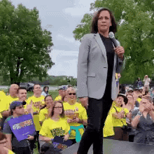 A Woman Stands On A Stage Holding A Microphone In Front Of A Crowd Of People . GIF