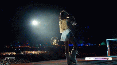 A Woman Stands On A Stage In Front Of A Crowd With A Sign That Says Coachella Stage GIF