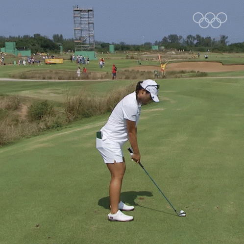 A Woman Swinging A Golf Club On A Golf Course With The Olympic Rings In The Background GIF