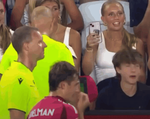 A Woman Takes A Picture Of A Man Wearing A Jersey That Says ' Elman ' On It GIF