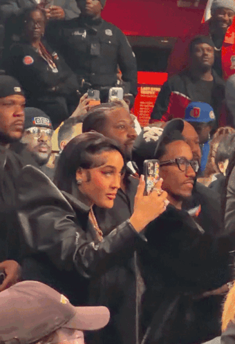 a woman taking a picture of a man wearing a hat that says ' der ' on it