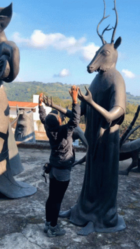 A Woman Taking A Picture Of A Statue With A Deer Head GIF