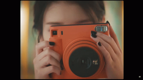 a woman taking a picture with an orange camera that says fuji