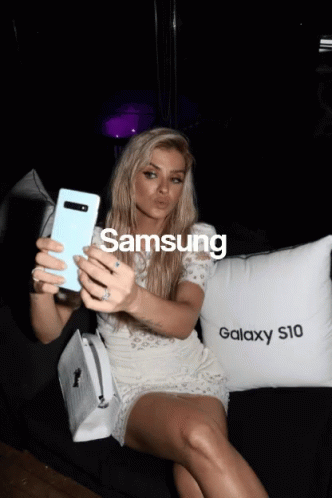 A Woman Taking A Selfie Next To A Pillow That Says Samsung GIF
