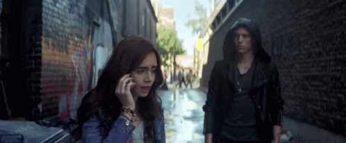 A Woman Talking On A Cell Phone While A Man Stands Behind Her GIF