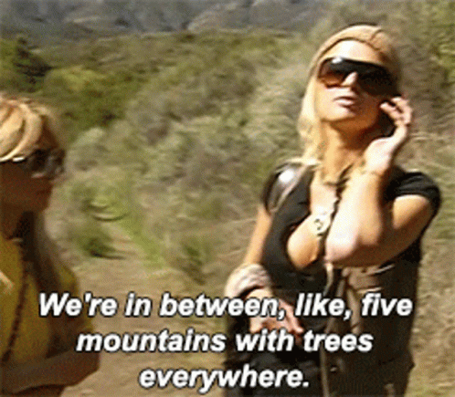 A Woman Talking On A Cell Phone With The Words We 'Re In Between Like Five Mountains With Trees Everywhere Above Her GIF