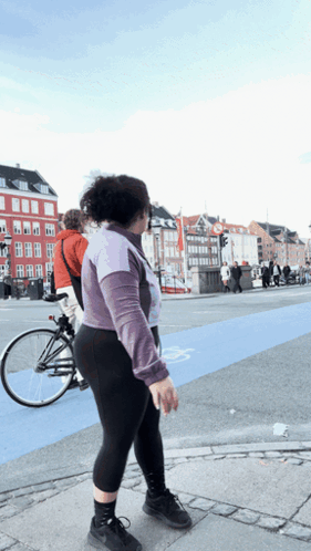 A Woman Walking Across A Street With A Bicycle Behind Her GIF